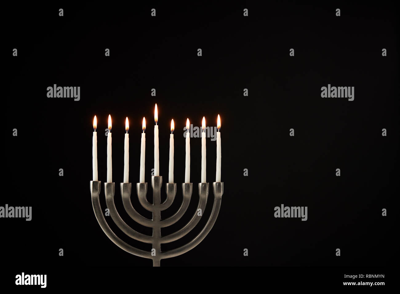 Lit Candles On Metal Hanukkah Menorah Against Black Studio Background Stock Photo