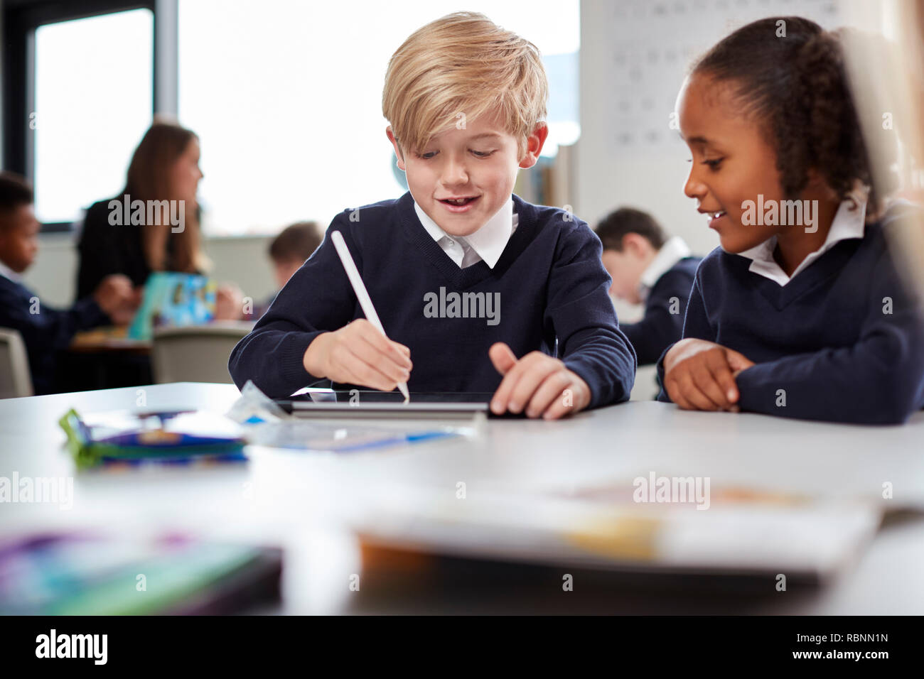 A girl and a boy using a tablet computer and stylus in a primary school class, front view, selective focus Stock Photo