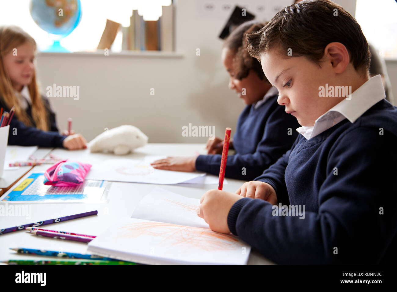 Pre-teen school boy with Down syndrome sitting at a desk writing in a primary school class, close up, side view Stock Photo
