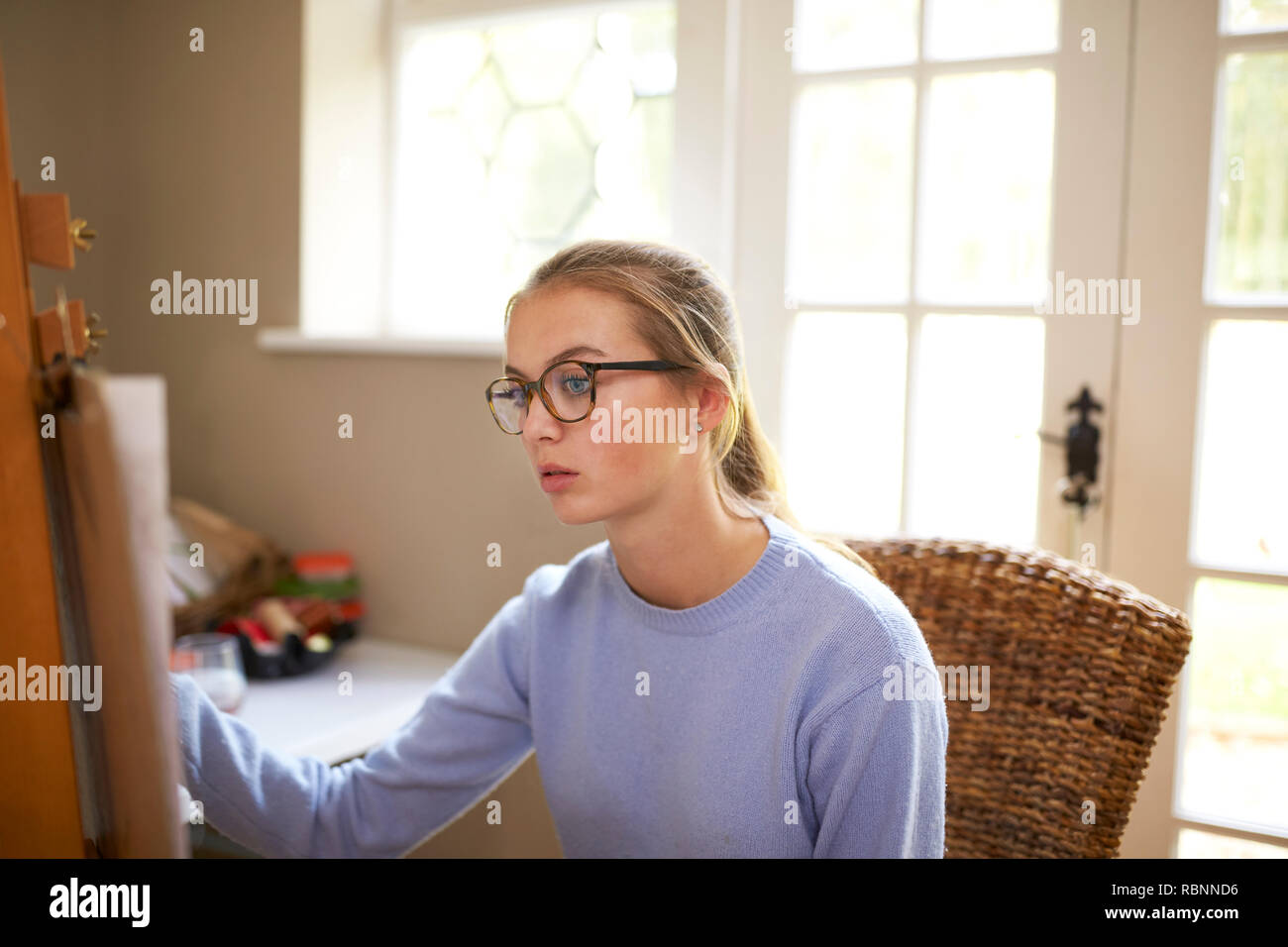 Female Teenage Artist Sitting At Easel Drawing Picture Stock Photo