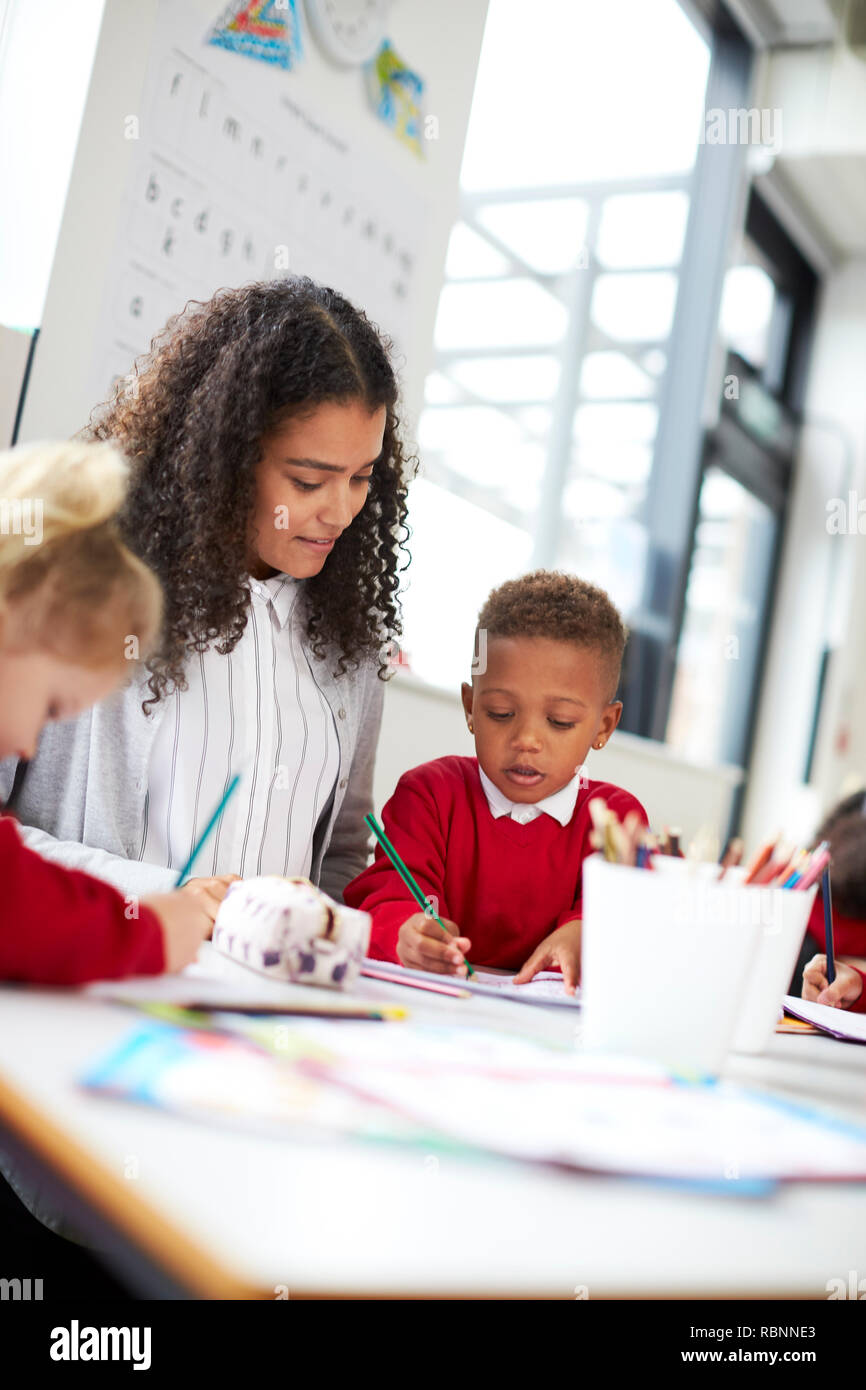 Two infant school kids and their female teacher sitting at table in a classroom drawing, low angle Stock Photo