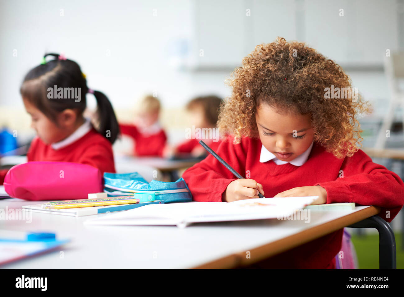 Schoolgirl sitting at a desk in an infant school classroom drawing ...
