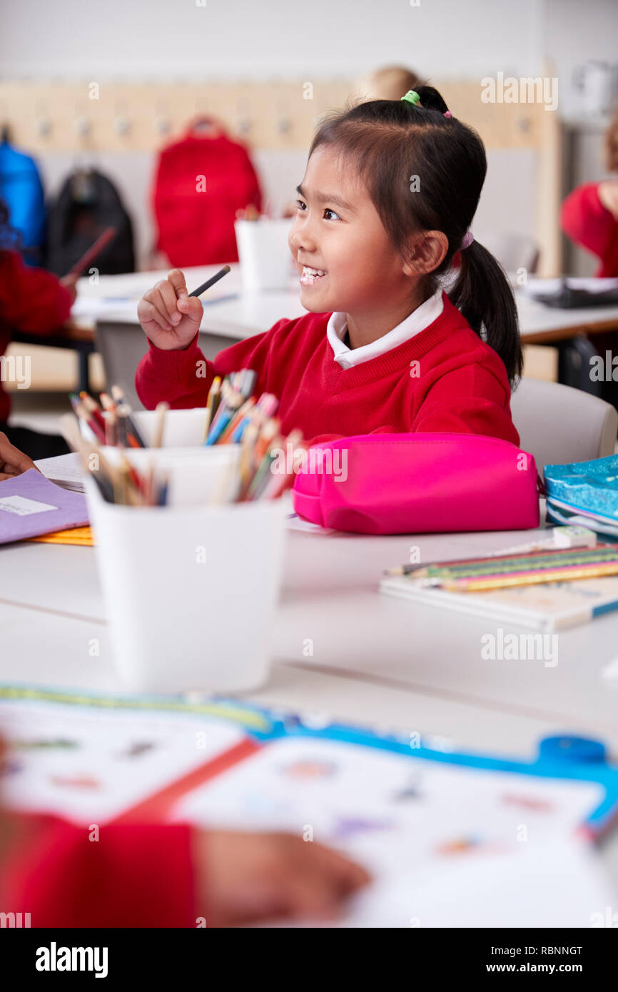 Close up of young Chinese schoolgirl wearing school uniform sitting at a desk in an infant school classroom, selective focus, vertical Stock Photo