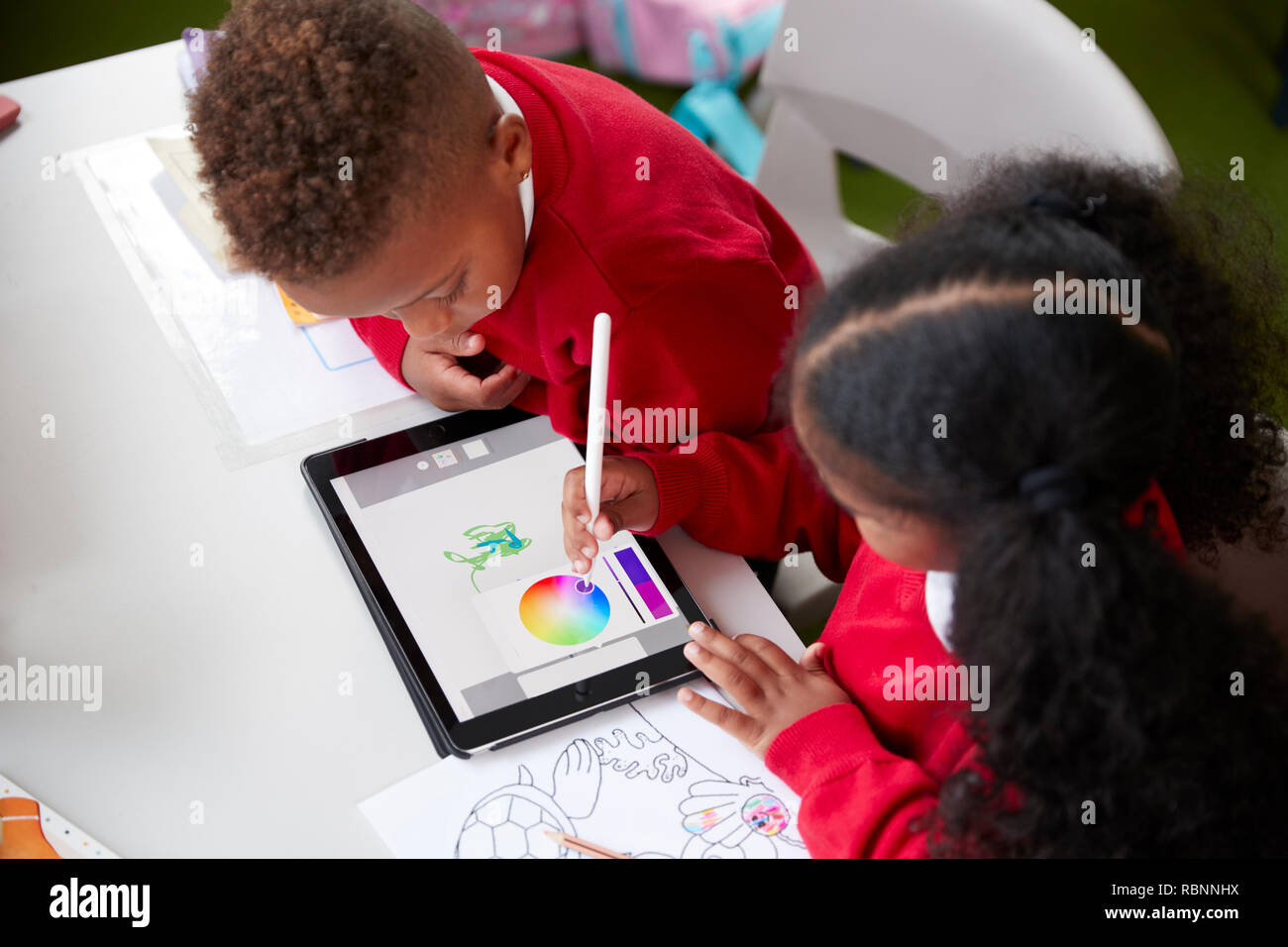 Elevated view of two kindergarten school kids sitting at a desk in a classroom drawing with a tablet computer and stylus, close up Stock Photo