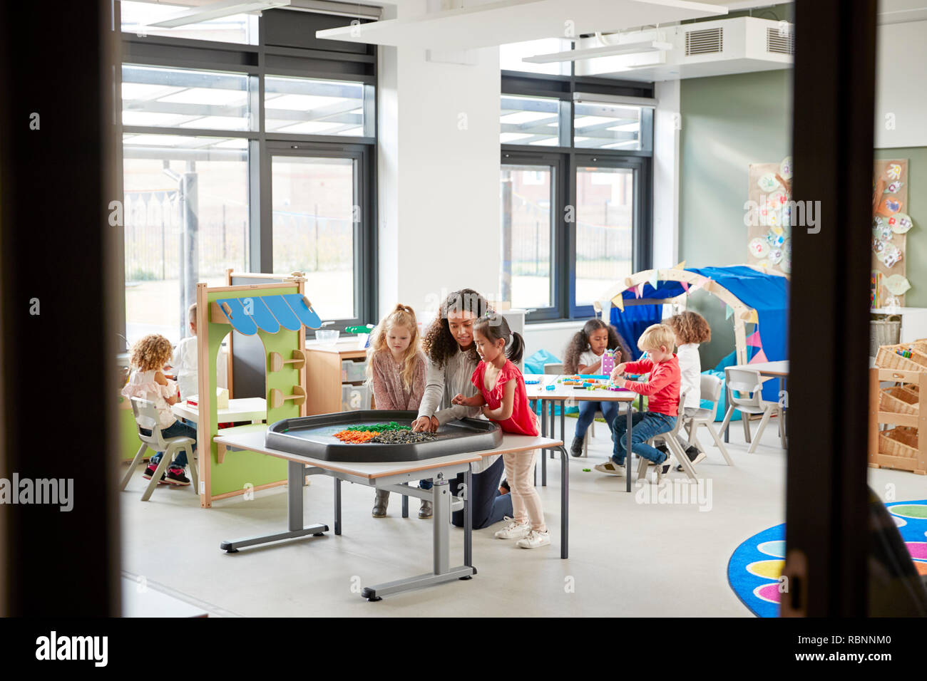 Kids playing games with a female teacher in a classroom in an infant school, seen from doorway Stock Photo