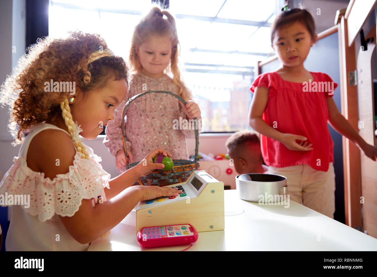Three kindergarten schoolgirls playing shop in a playhouse at an infant school, backlit Stock Photo