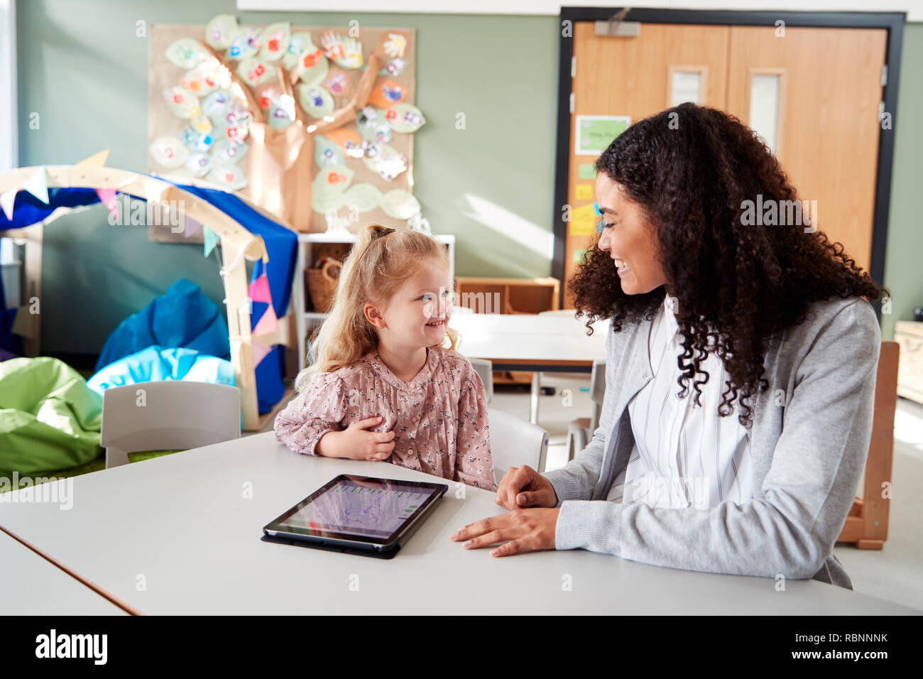 Young white schoolgirl working one on one together in a classroom with a female infant school teacher, smiling at each other, close up Stock Photo