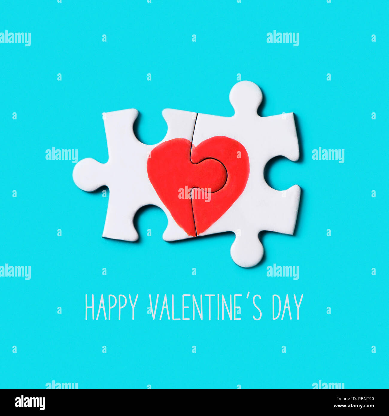 closeup of two pieces of a puzzle forming a heart and the text happy valentines day on a blue background Stock Photo