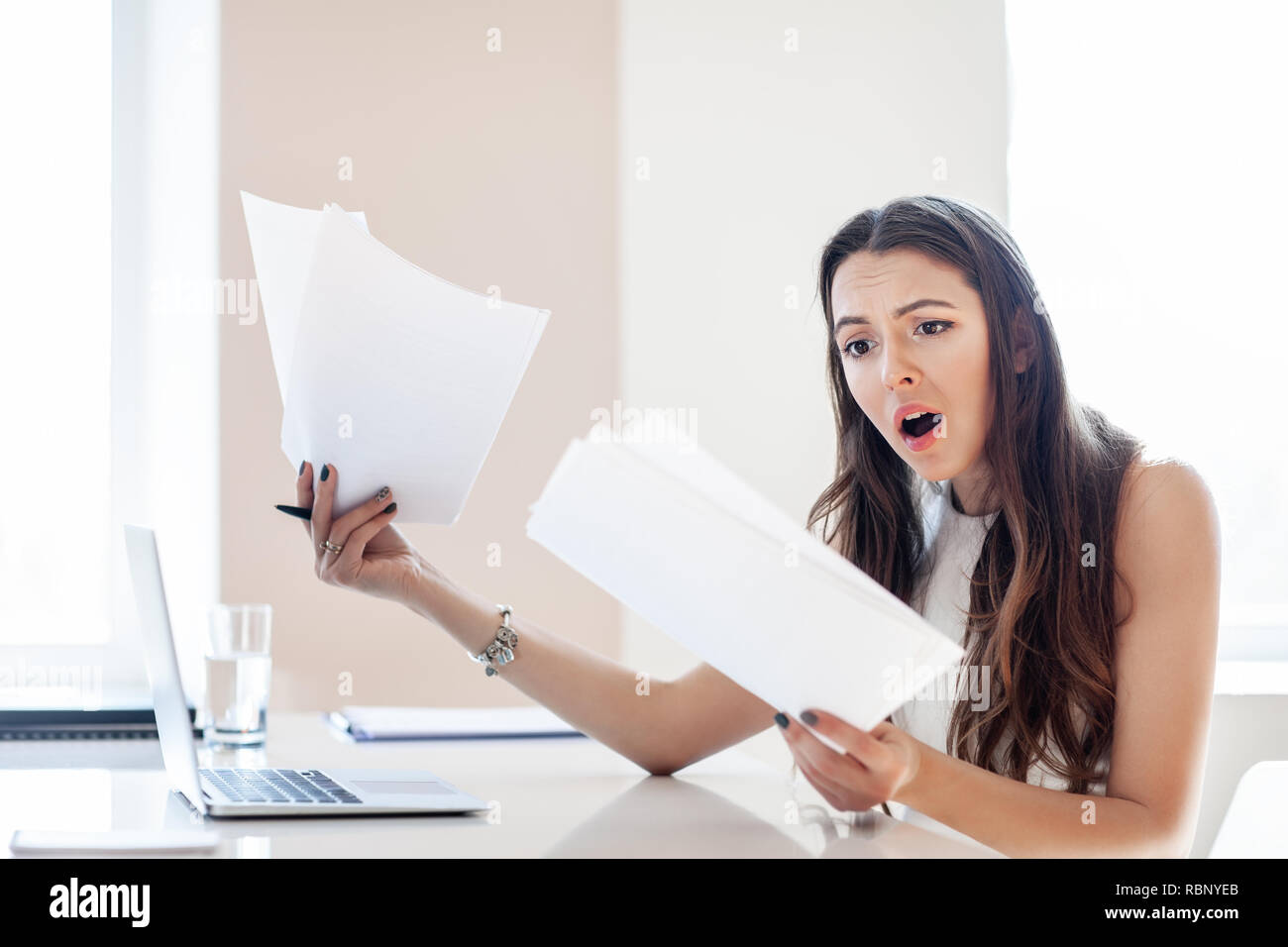 Shocked businesswoman reading paper at workplace in office. Business woman frustrated and stressed with new contract Stock Photo