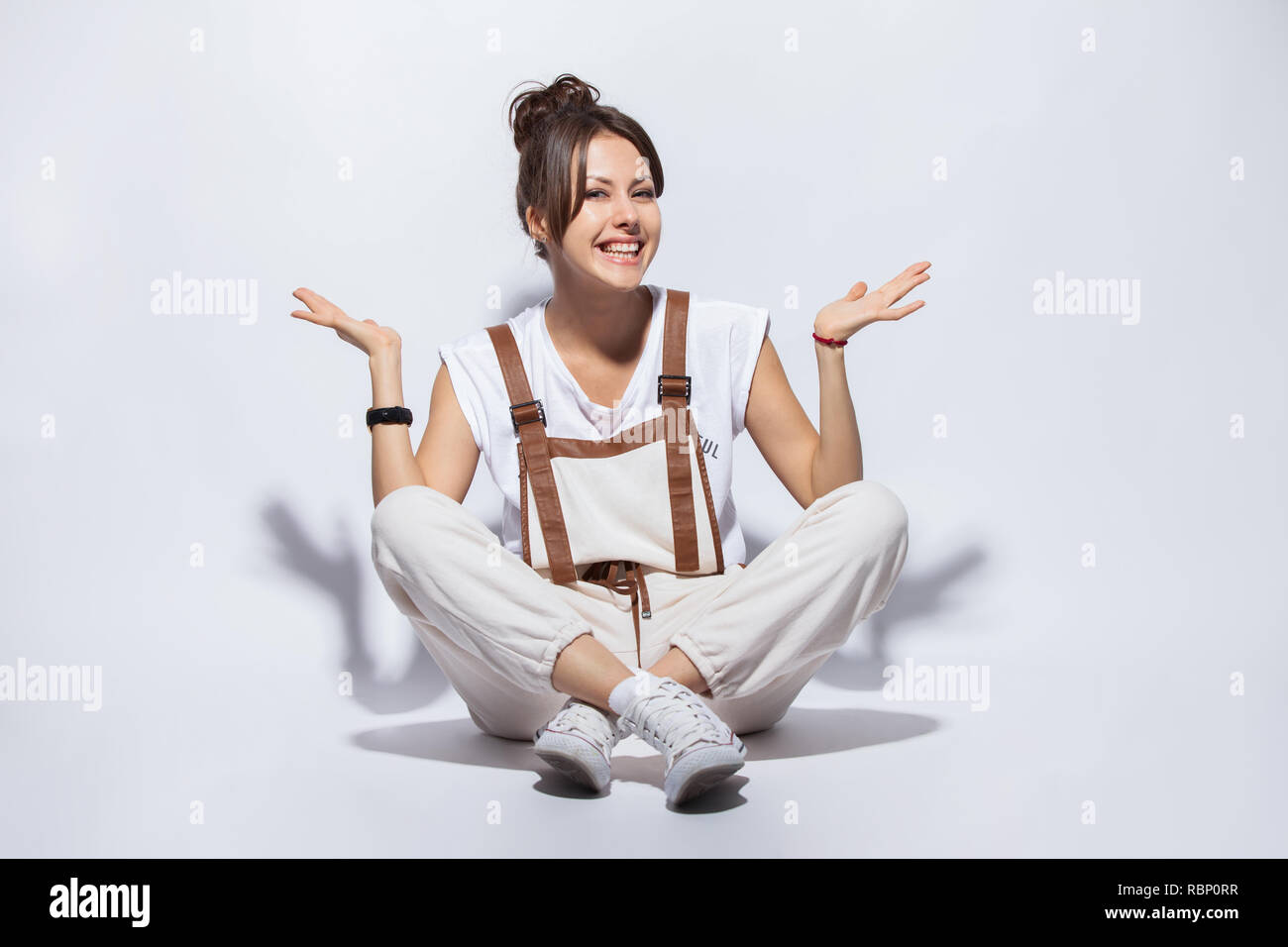 Portrait of a casual happy woman sitting on the floor on white background. Stock Photo