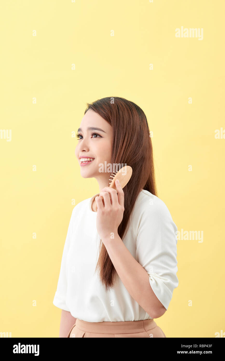 Portrait of cute young woman on yellow background combing hair. Stock Photo