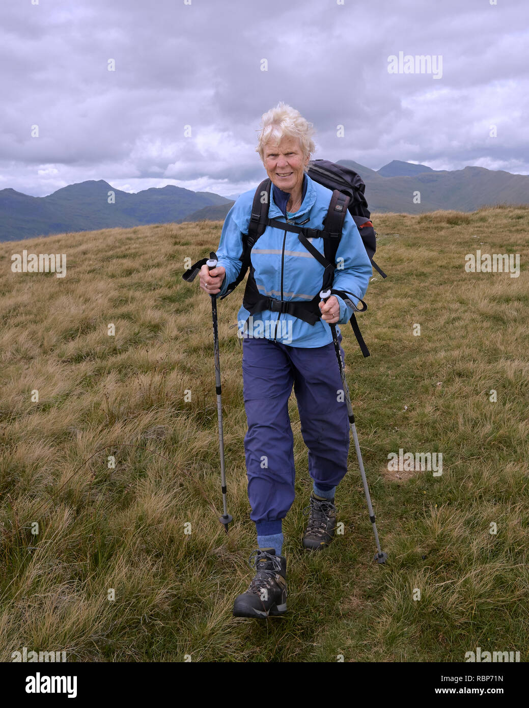 Woman hill walking with walking poles, dressed in blue.  Stob Fear-tomhais, Balquhidder, Stirling, Scotland Stock Photo