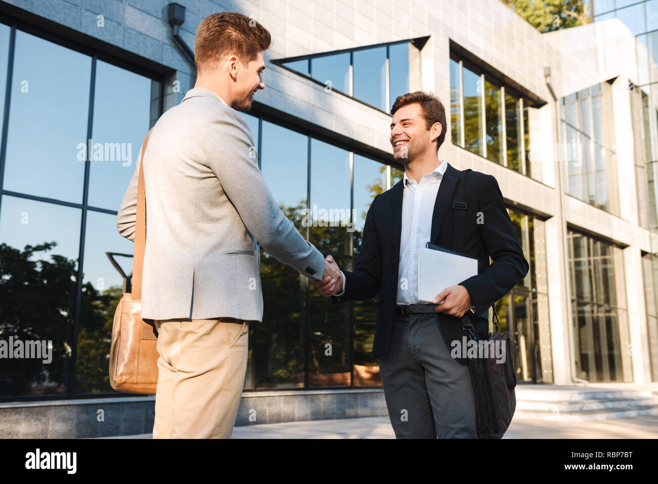 Two confident businessmen standing outdoors, shaking hands Stock Photo