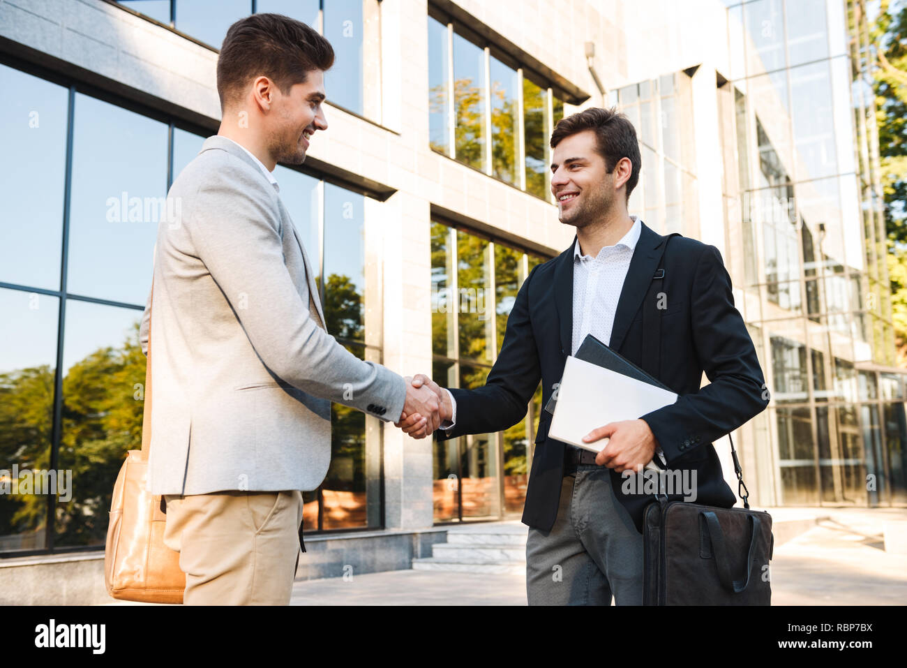 Two confident businessmen standing outdoors, shaking hands Stock Photo