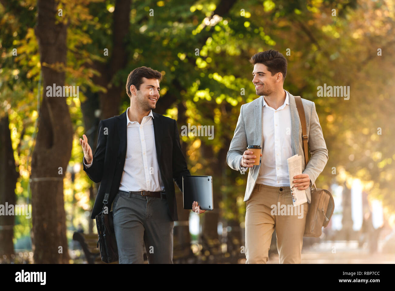 Two happy businessmen walking outdoors, drinking coffee, talking Stock Photo