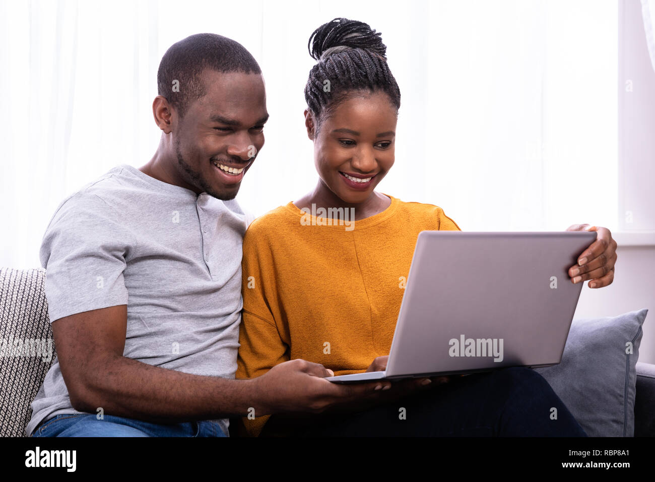 Happy Young Couple Sitting On Sofa Using Laptop Stock Photo