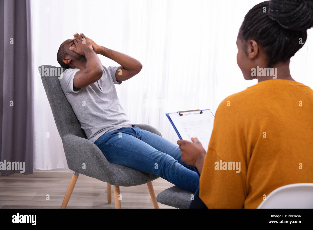 Female Psychologist With Clipboard Sitting Near Young Man Suffering
