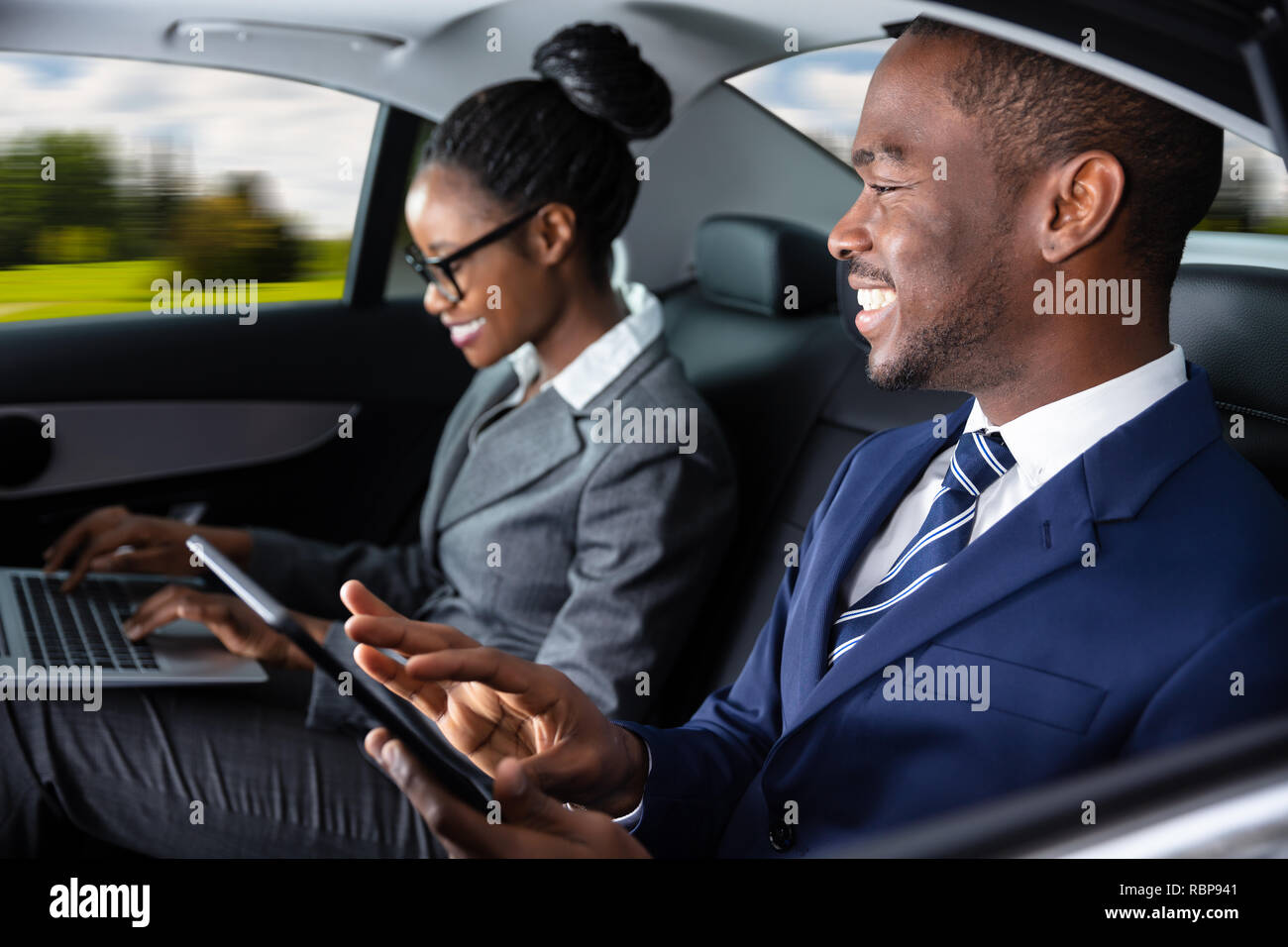 Two Happy African Businesspeople Using Electronic Devices While Traveling By Car Stock Photo