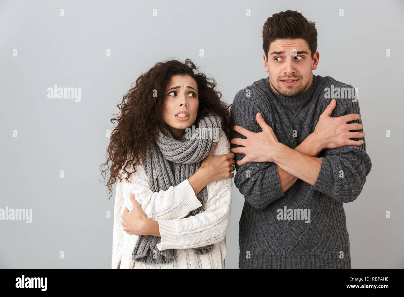 Photo of displeased couple man and woman wearing scarfs trembling and hugging themselves isolated over gray background Stock Photo