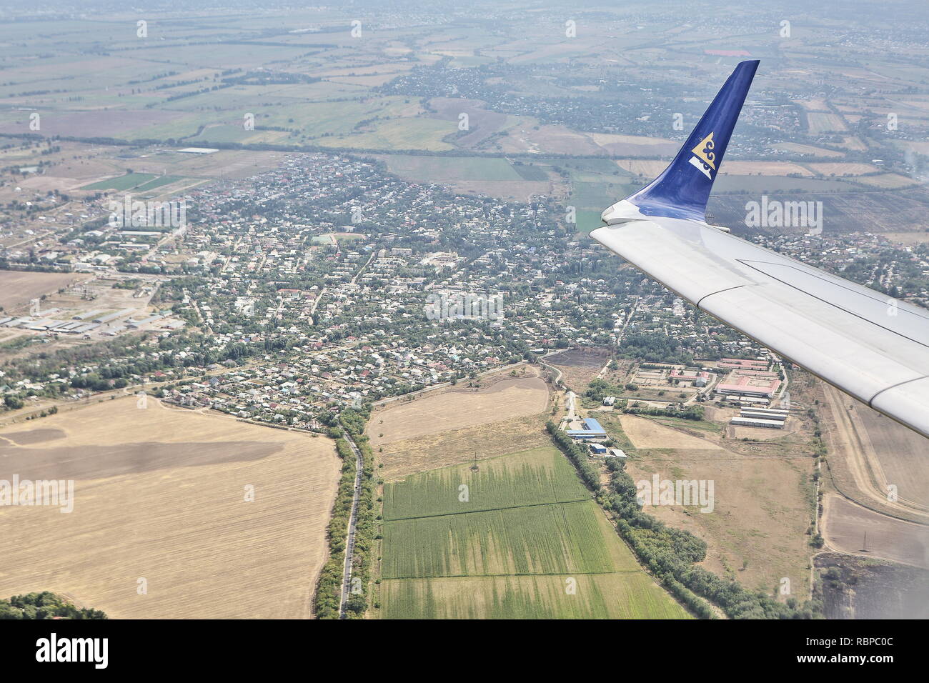 A wing of Kazakh Air Astana Embraer jet carrier flying over Kazakh city Pavlodar suburban areas, very efficient regional carrier model made in Brasil. Stock Photo