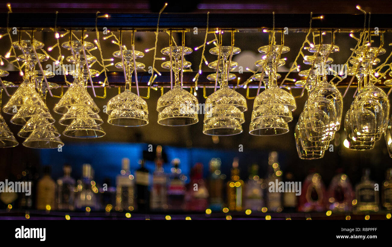 Twinkling fairy lights are caught in sparkling glassware hanging above a bar Stock Photo
