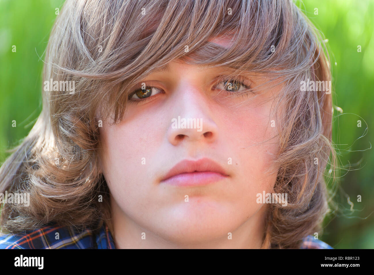 A close up portrait of a youg boy with long hair looking at camera. Stock Photo