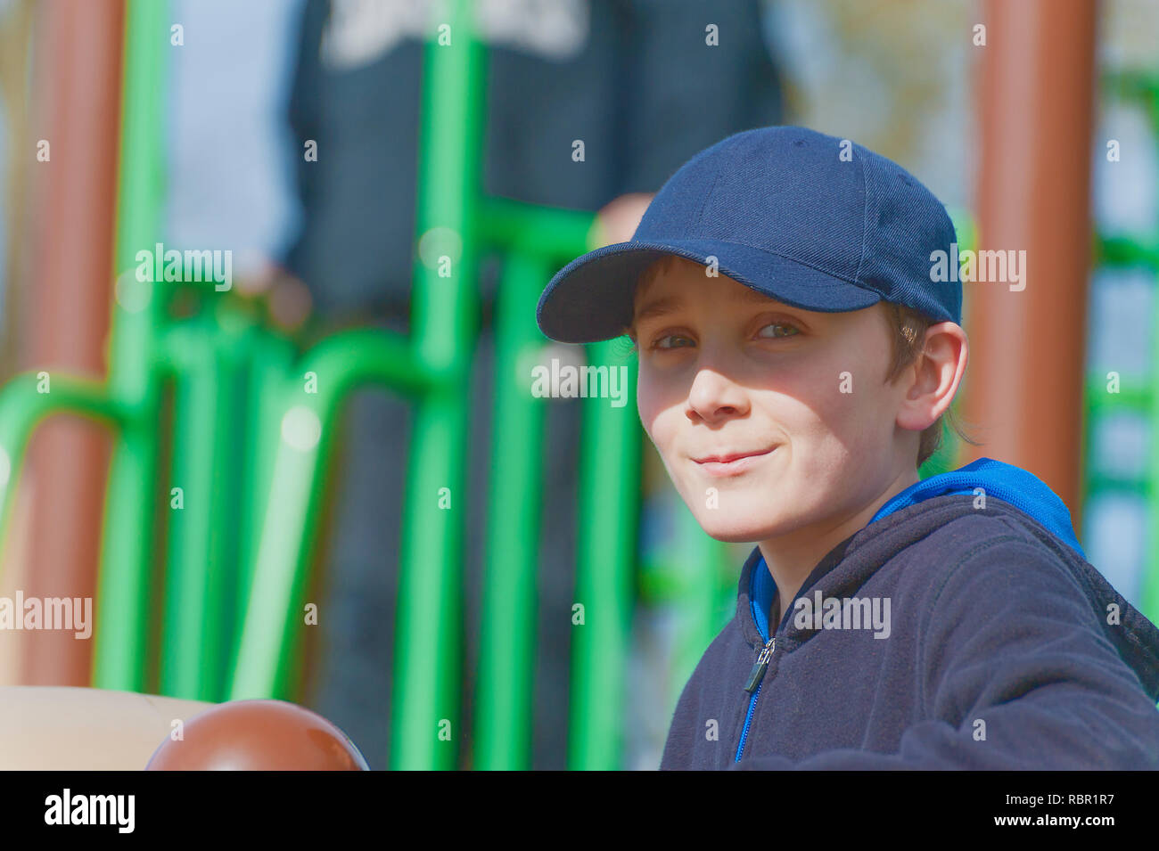 A young boy in a playground on a sunny day wear a blue ball cap. Stock Photo
