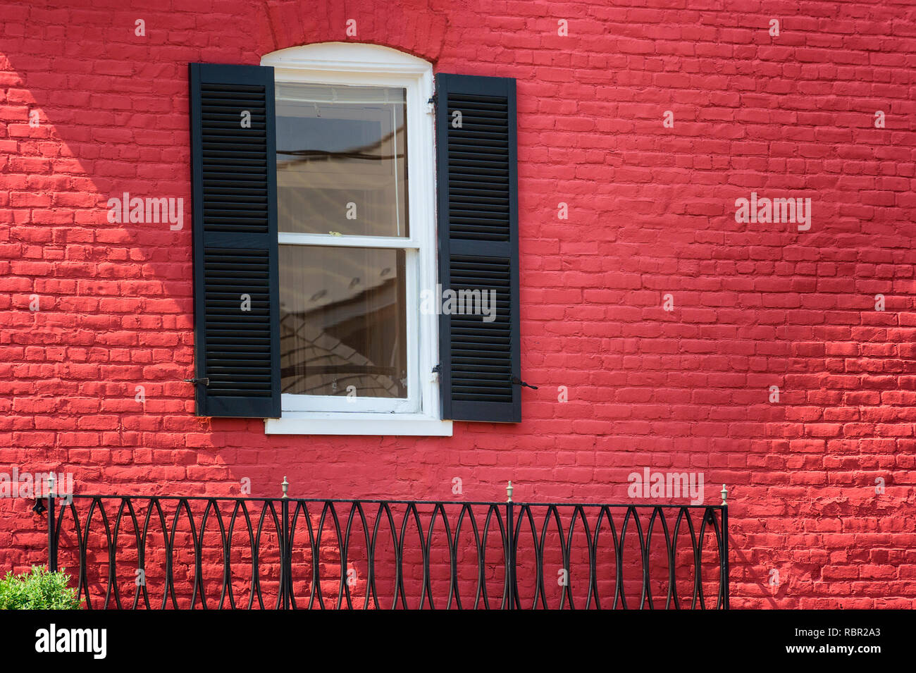 An exterior side of a red brick building with an iron railing, window framed with black shutters Stock Photo