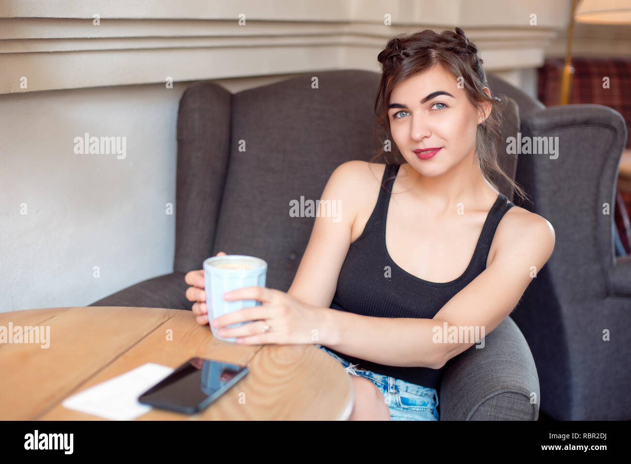 Young attractive girl in a black Tshirt and jeans sits in a cafe at
