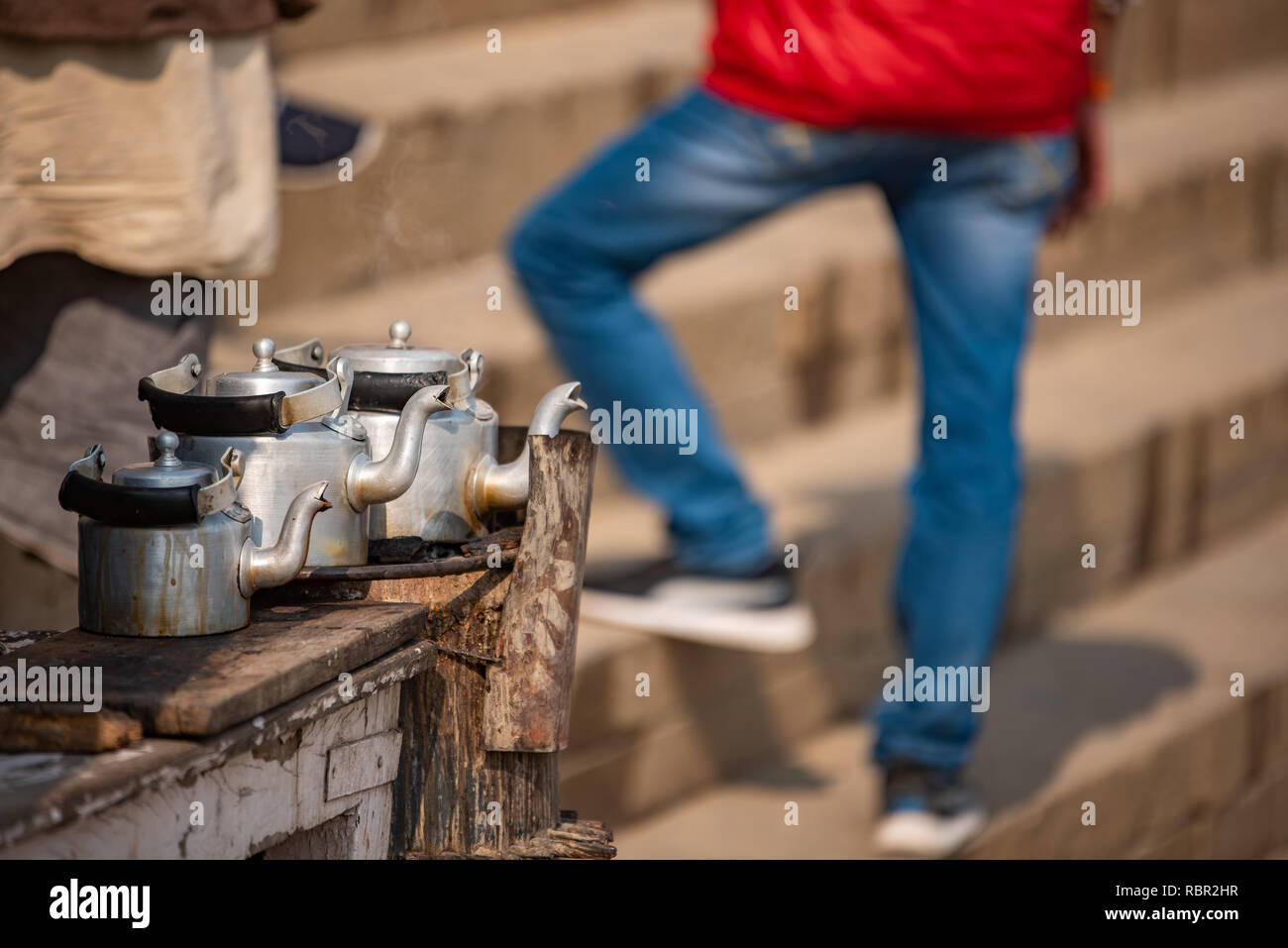 Three tea kettles and two legs in Varanasi, India: A man in a red top and blue jeans stands in the background while three tea kettles simmer away. Stock Photo