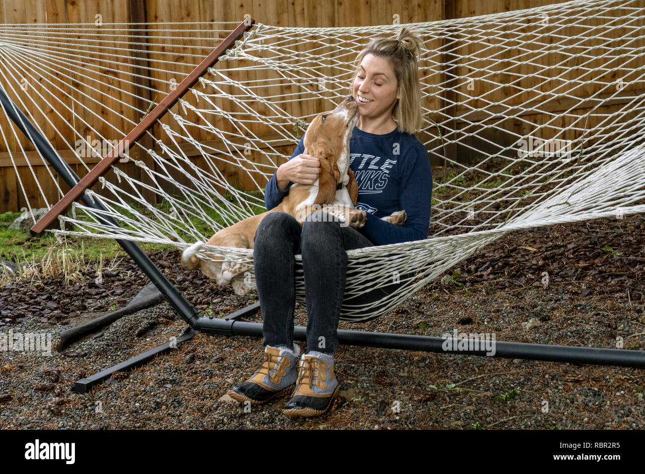 Renton, Washington, USA.  Woman being affectionate with her five month old Basset Hound puppy 'Elvis' as they rest in a  hammock. Stock Photo