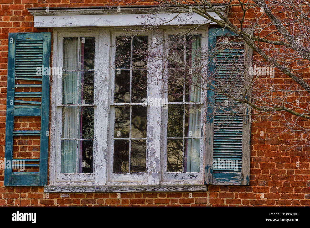 Decaying shutters on a paint peeling window that is part of a brick structure. Stock Photo