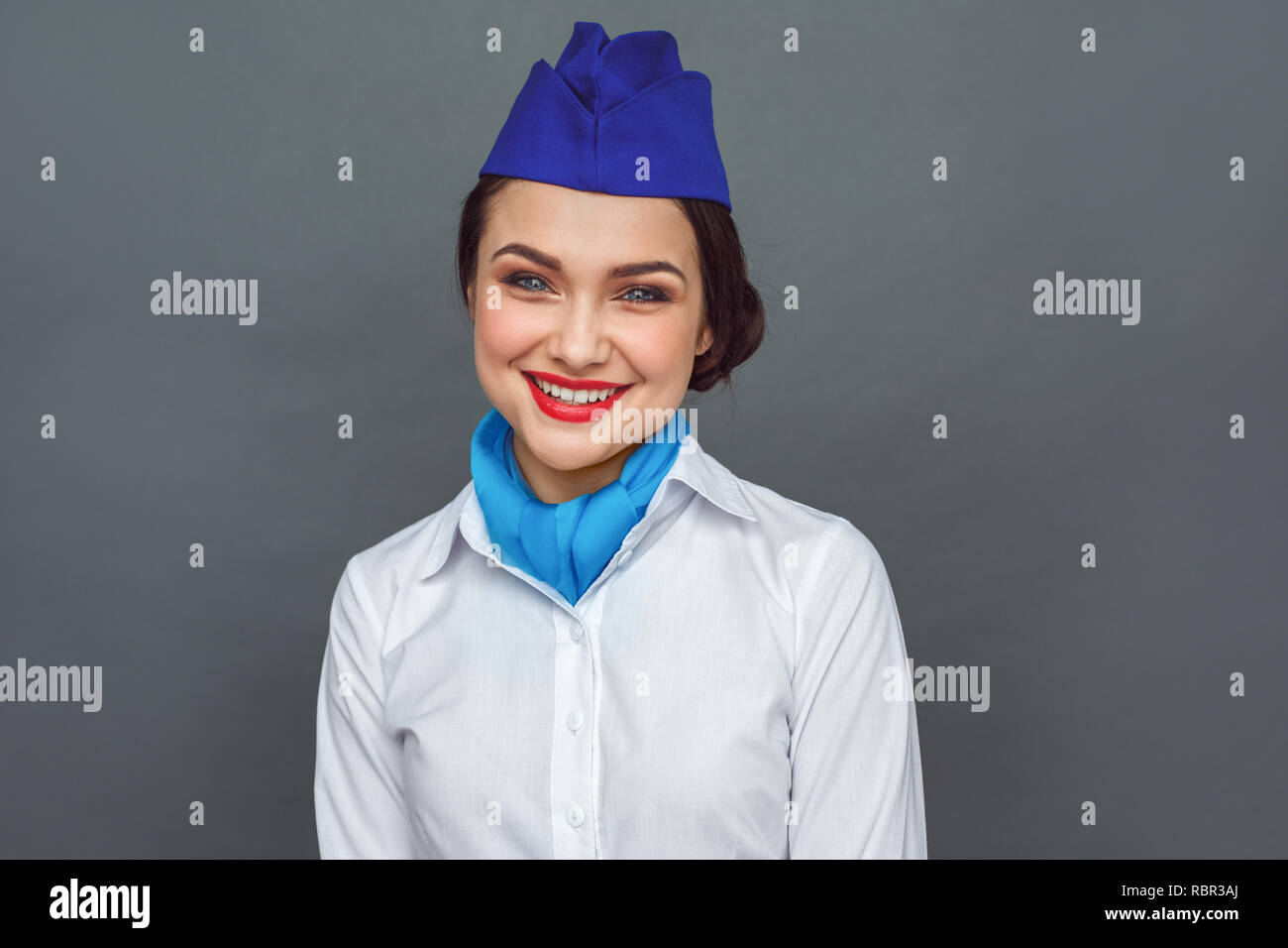 Young woman professional stewardess standing isolated on grey wall looking camera smiling friendly Stock Photo