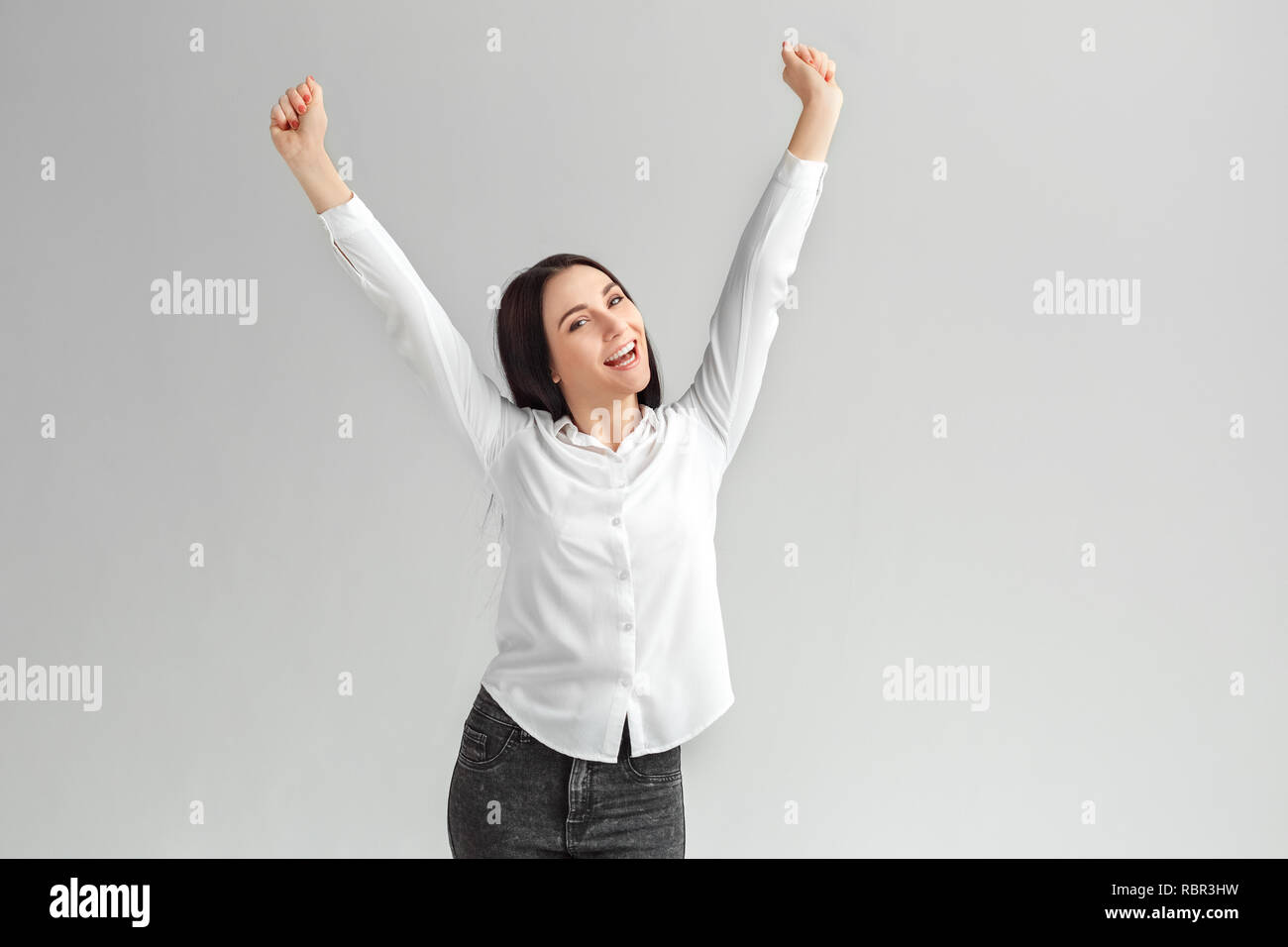 Young woman studio standing isolated on gray wall hands up success ...