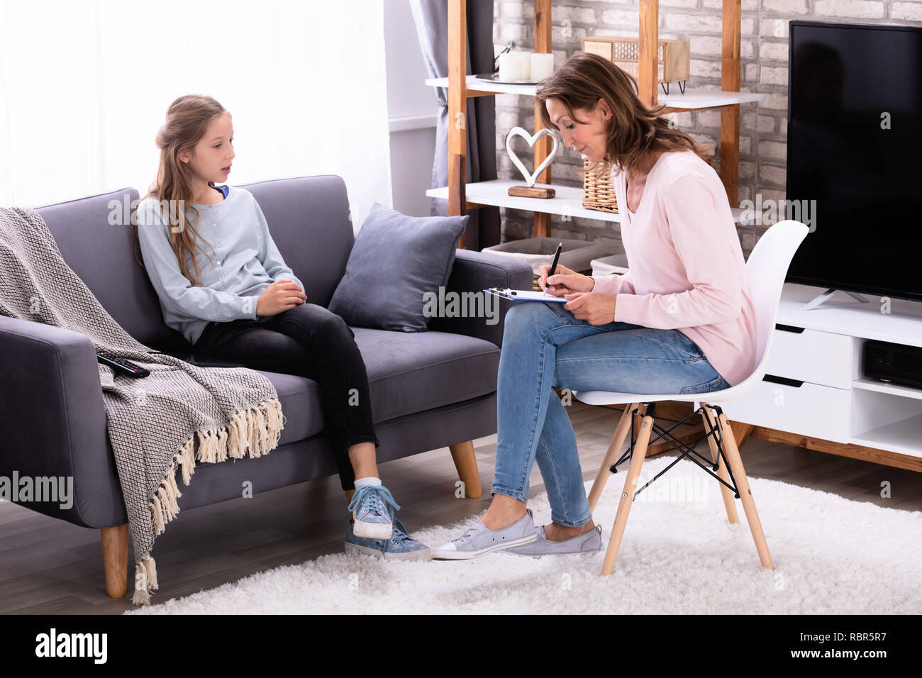Girl Sitting On Sofa Explaining Her Problems To Female Psychiatrist At Home Stock Photo
