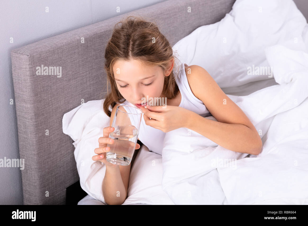 Girl Lying On Bed Taking Medicine With Glass Of Water Stock Photo