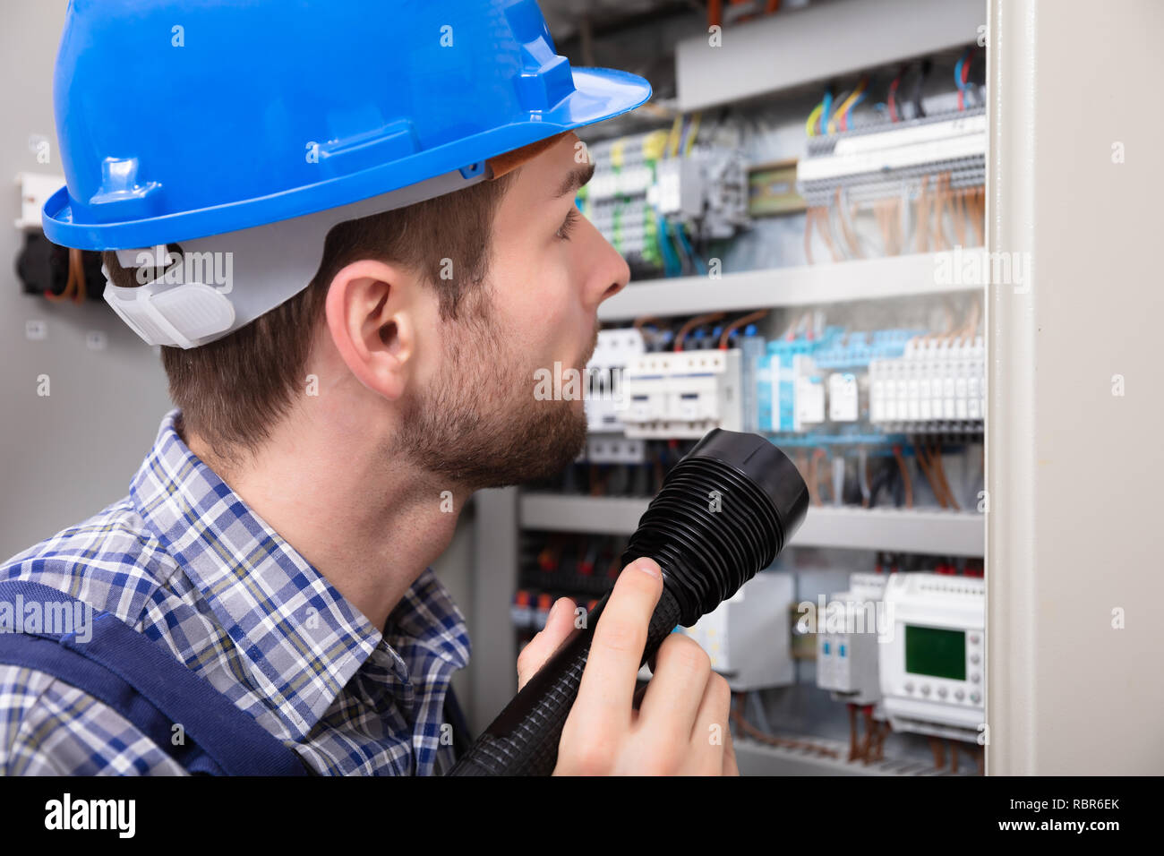 Close-up Of A Electrician Examining A Fuse Box With A Torch Stock Photo