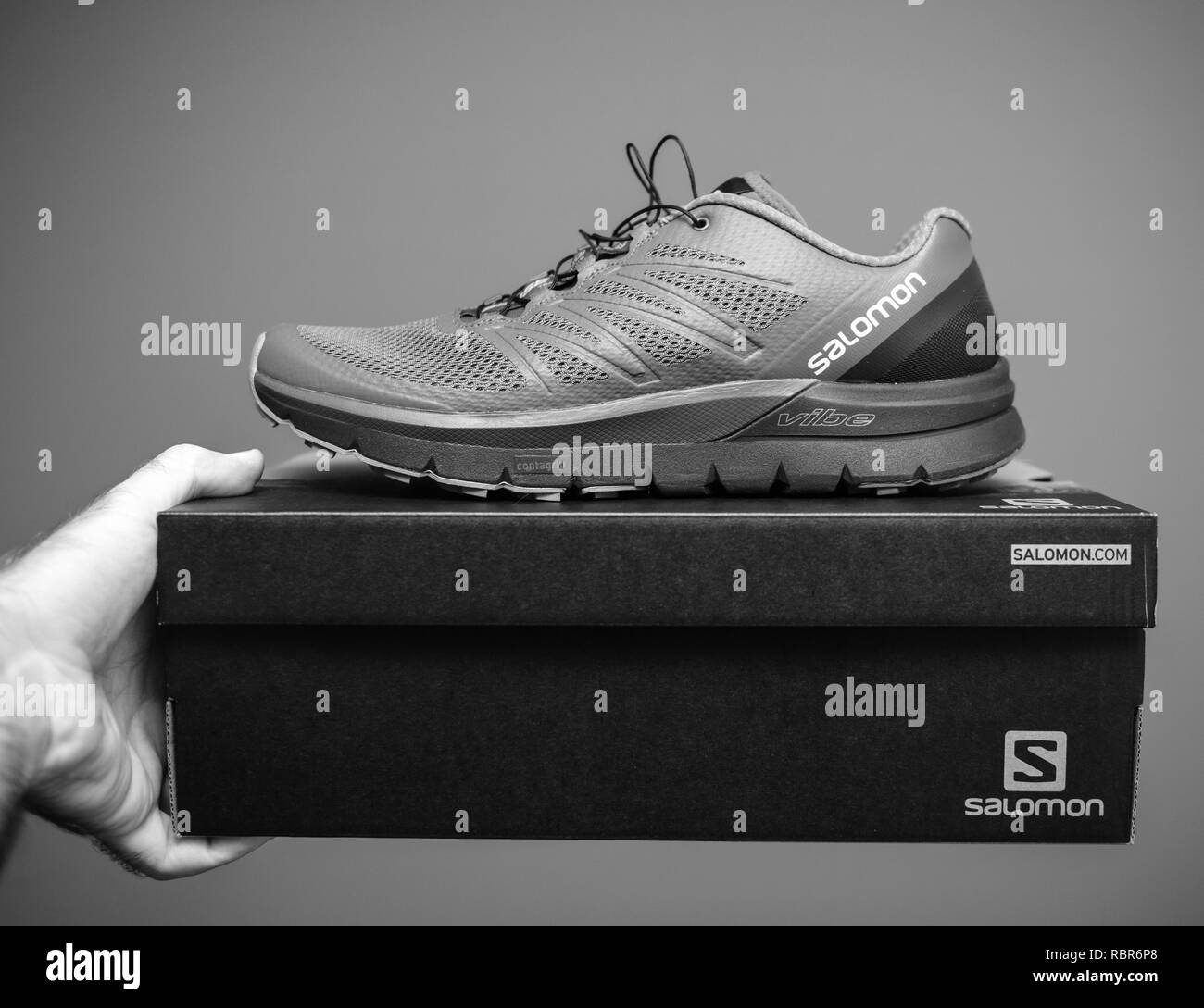 PARIS, FRANCE - NOV 22, 2018: Man holding against gray background a box  with a pair of new Salomon Sense Pro Max everyday trail running performance  with maximum cushioning black and white