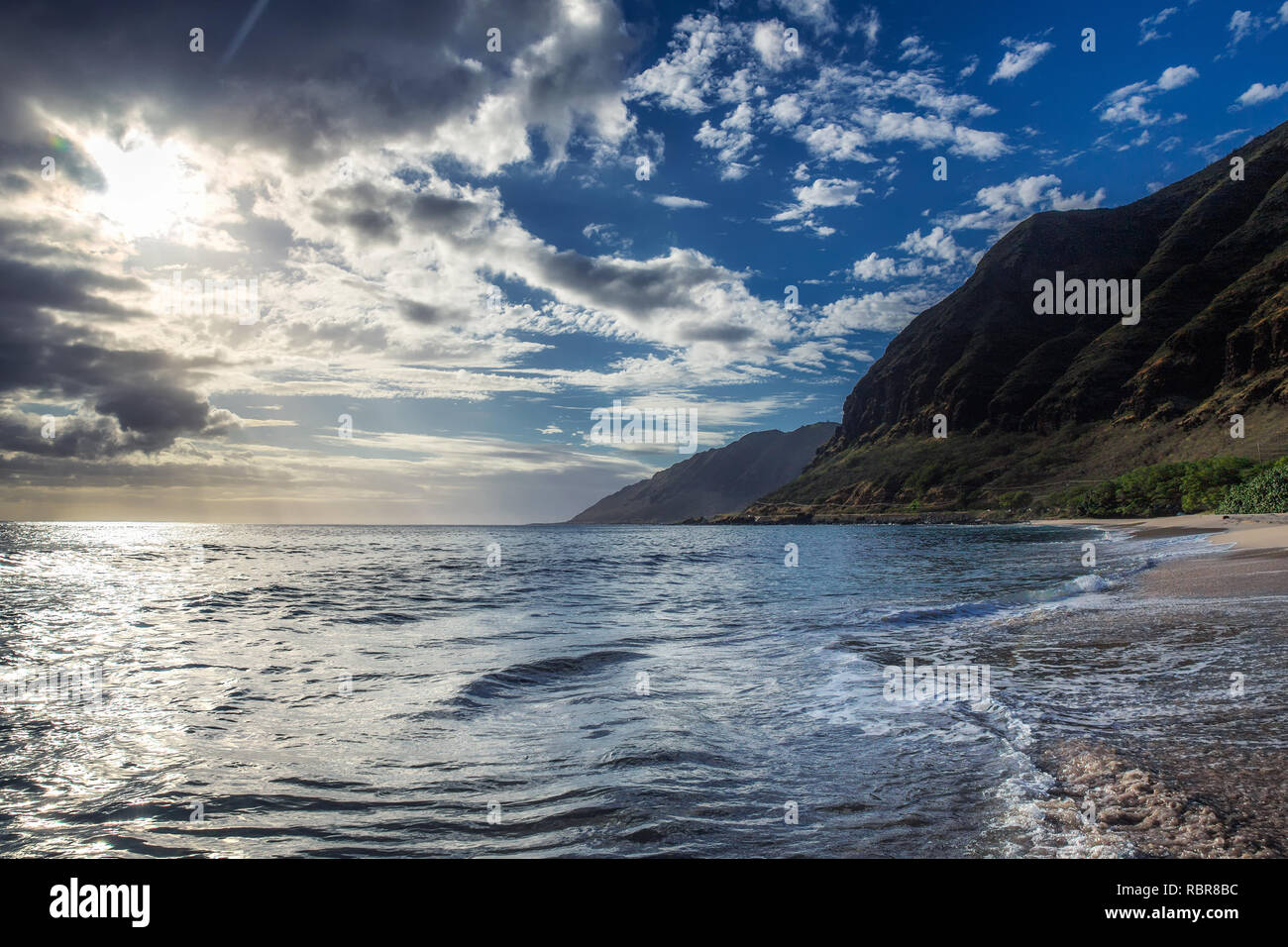 Sun shining through the clouds at sandy beach with waves Stock Photo