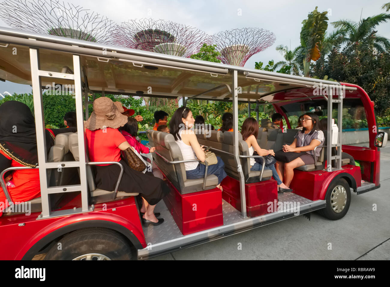 Tourists on a shuttle bus in Gardens by the Bay, Marina Bay, Singapore; background some of the