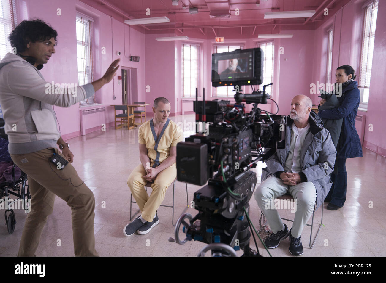 (from left) Writer-director M. Night Shyamalan, James McAvoy, who plays Kevin Wendell Crumb/The Horde, Bruce Willis, who plays David Dunn/The Overseer, and a crew member, on the set of 'Glass,' written and directed by M. Night Shyamalan. Photo Credit: Universal Pictures / The Hollywood Archive Stock Photo