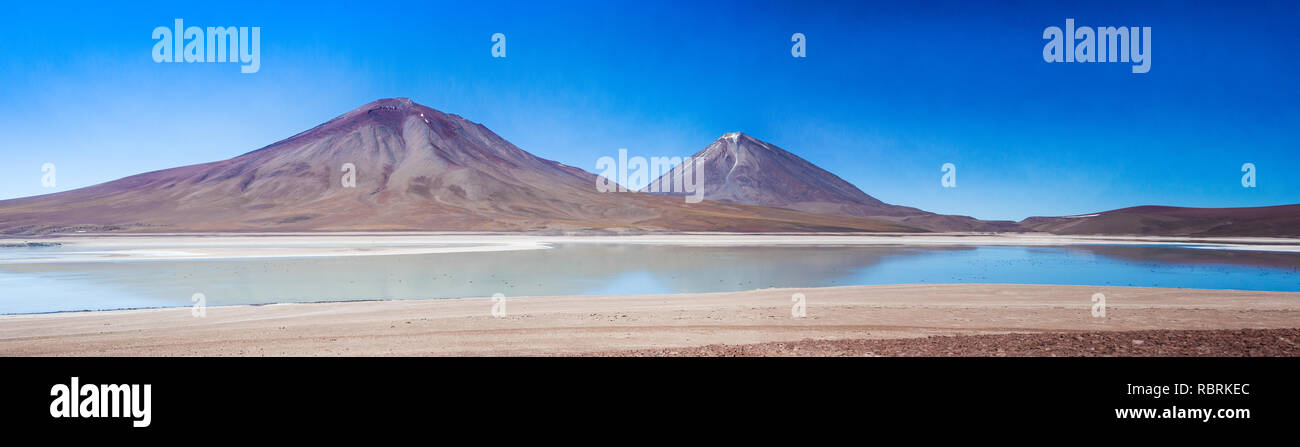 A calming and peaceful panoramic scene of the mountains forming the border between Chile and Bolivia reflected in the still waters of Laguna Verde. Stock Photo