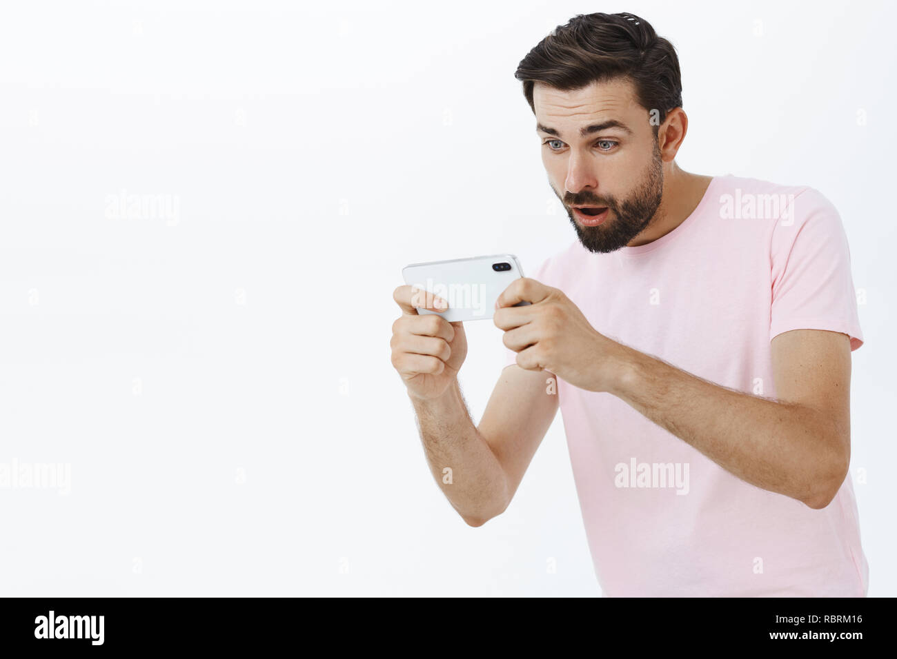 Adult bearded man playing amusing game via smartphone holding mobile phone  with both hands looking focused and excited at cellphone screen entertained  with cool app over gray background Stock Photo - Alamy