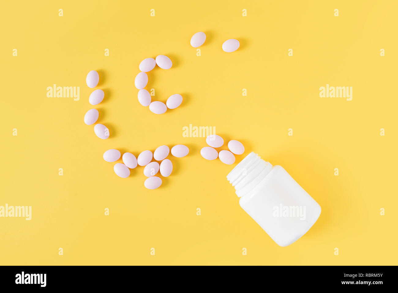 Vitamin c pills dropped from bottle on yellow background. Flat lay, top