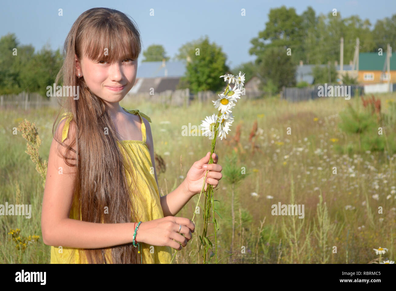 Happy teen girl at summer meadow, collecting flowers, telephoto shot Stock Photo