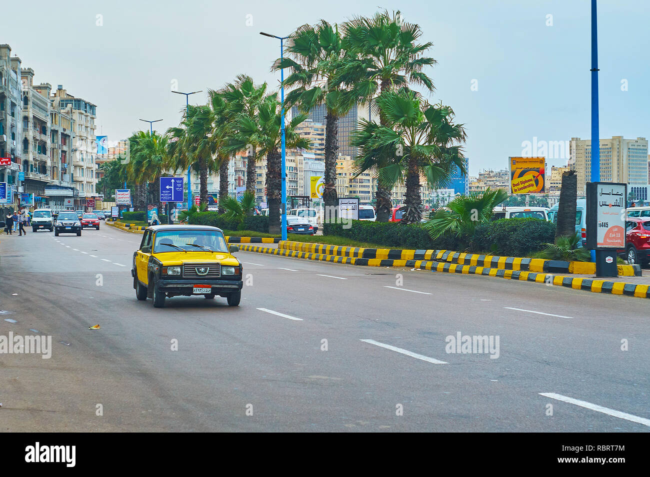 ALEXANDRIA, EGYPT - DECEMBER 19, 2017: The vintage taxi drives along the Corniche Avenue with a line of green palms on the background, on December 19  Stock Photo