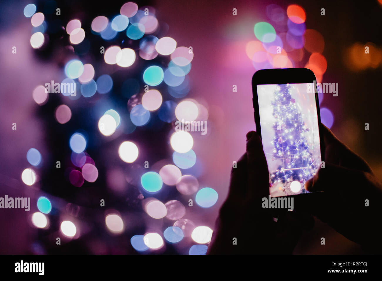 Man holding a phone and taking a picture of the Christmas tree lamps Stock Photo