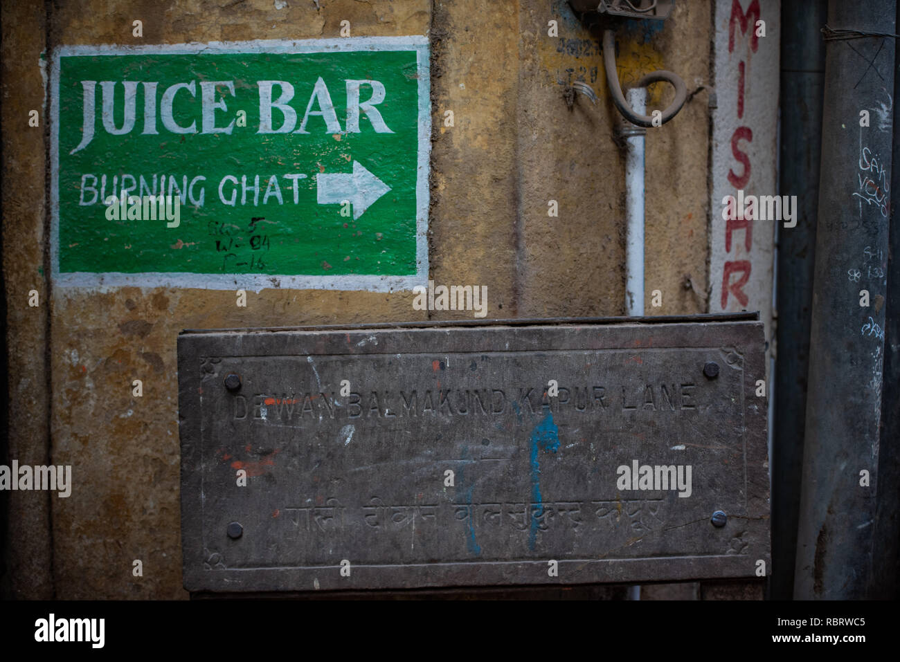 Painted sign in Varanasi pointing to a 'Juice Bar' and 'Burning Ghat' or a cremation area together highlights the macabre reality of the city. Stock Photo