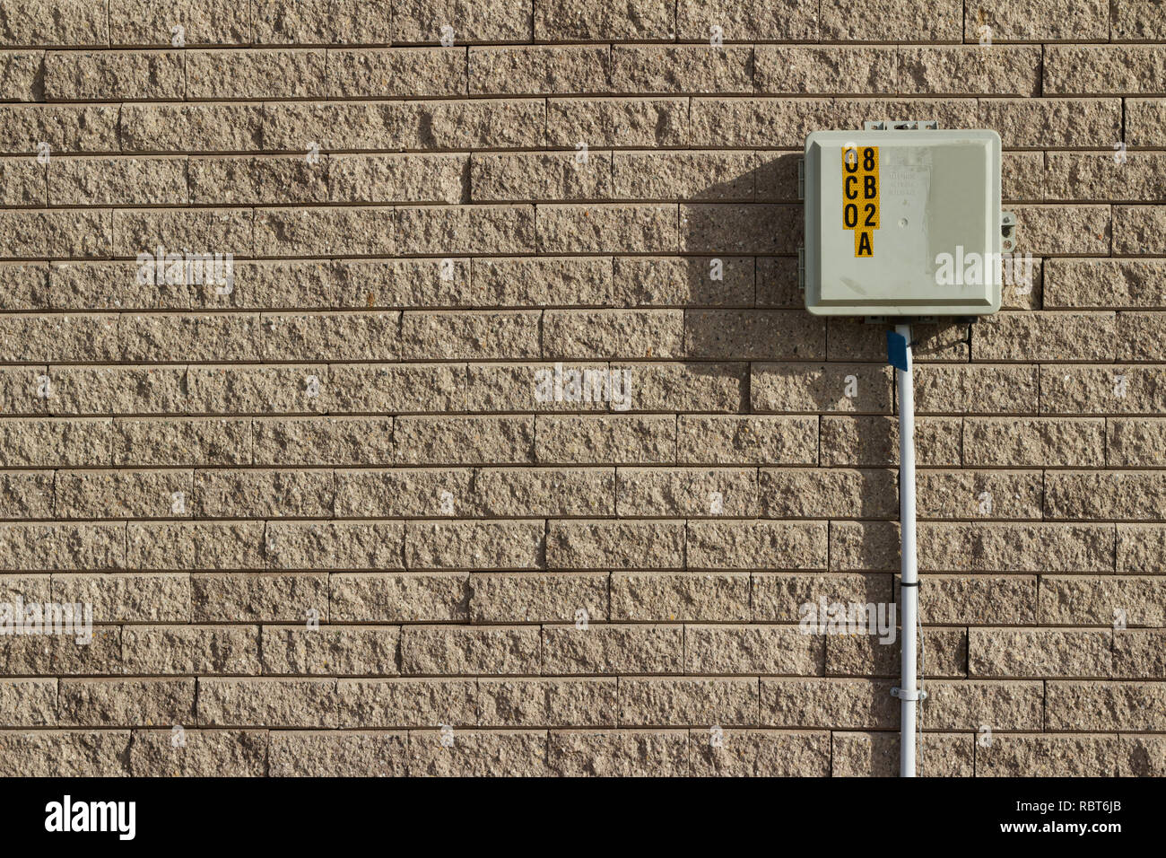 Light brown tan colored rough textured stone brick wall abstract background with attached telephone utility box and pole Stock Photo
