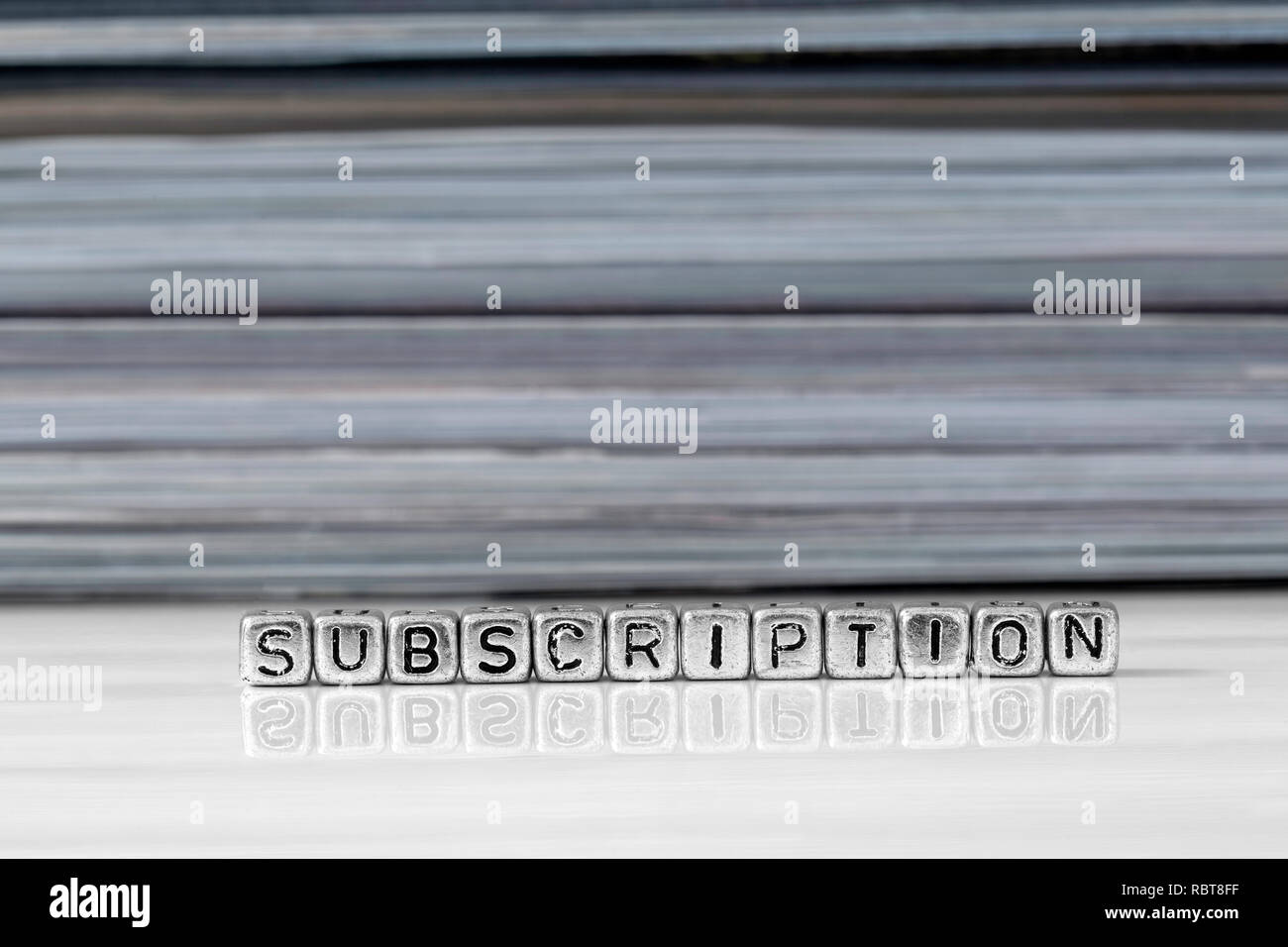 Subscription on beads with magazines stacked in the background reflected on a white surface Stock Photo